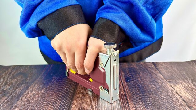 Person blue clothing using a staple gun to secure a wooden surface