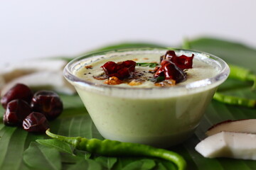 Two bowls of spicy coconut chutney, styled with coconut slices, green chilies, and curry leaves as...