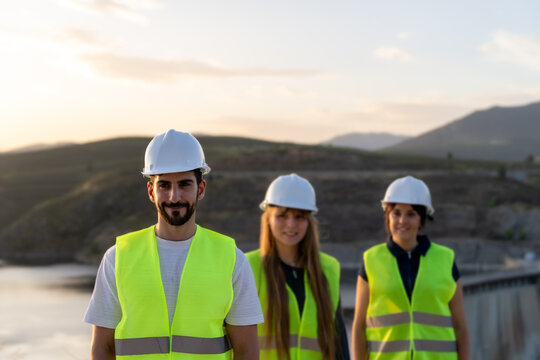 Engineers wearing safety vests and helmets working at sunset near a dam - Powered by Adobe