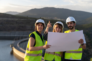 Engineers reading blueprint and discussing while pointing at dam