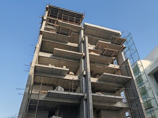 Under construction residential building Block structure. Highrise Incomplete Modern Design Tower with Top Level View. Multi Story Residential Site with erected Scaffolding Pipes around the Building. 