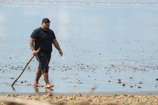 Man walking barefoot with stick on rocky beach shore