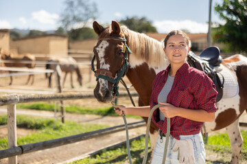 Young woman leading horse by bridle in paddock