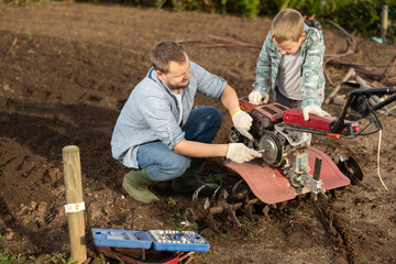 Male farmer and his son are repairing a cultivator to cultivate the land on the farm. Farmer...