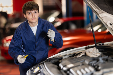 Qualified mechanic in a car service checks the amount of oil in the car with a dipstick. Car...