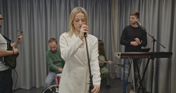 Music band practicing together in a rehearsal studio before a concert. The female lead singer is singing while the other members play their respective instruments.