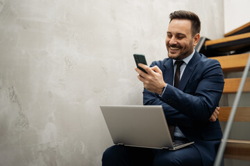 Businessman sitting on stairs and using laptop and smartphone