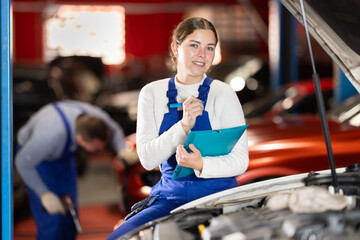 Female car service worker fills out papers and recommendations for car repairs. Mechanic draws up a...