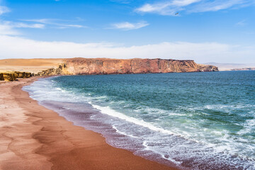 A breathtaking view of Playa Roja, known for its unique red sand and the dramatic cliffs in Paracas Natural Reserve.