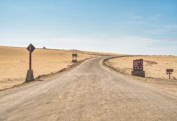 A lonely paved road with direction signs on the sides in the arid desert landscape of Paracas National Reserve in Peru.
