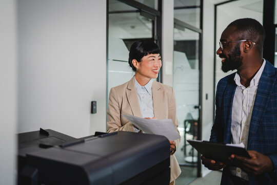 Two multicultural businesspeople talk while scan documents on a scanner