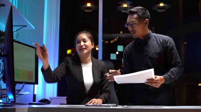 Modern Workplace Dialogue: A pair of dedicated professionals engages in a focused discussion, lit by the glow of computer screens.