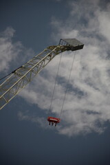 crane with hanging cables seen from below with a partially cloudy sky in the background 