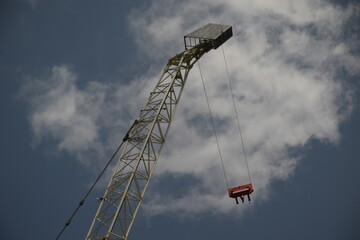 crane with hanging cables seen from below with a partially cloudy sky in the background 
