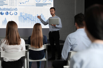 Business trainer giving lecture using video projector in conference room. Graphs on projection screen