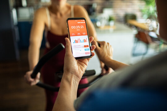 Senior lesbian couple tracking cardio workout progress on fitness app during exercise bike session