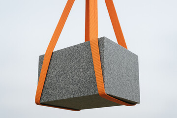 Heavy granite block securely lifted by bright orange straps against a clear sky, showcasing industrial strength and construction safety