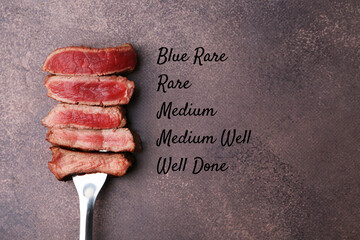 Pieces of delicious beef meat in different degrees of doneness on brown table, top view