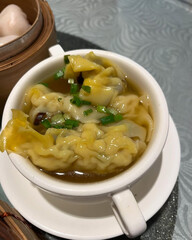 Wonton dumplings floating in hot soup bowl.