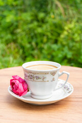 A cozy scene of a coffee cup and a pink rose on a rustic table, ideal for morning or lifestyle images.