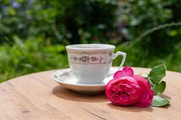 A cup of warm coffee with a pink rose on a rustic table, capturing a serene morning atmosphere.