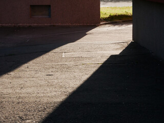 sun beam between the shadow of two buildings marking a gateway on the road surface