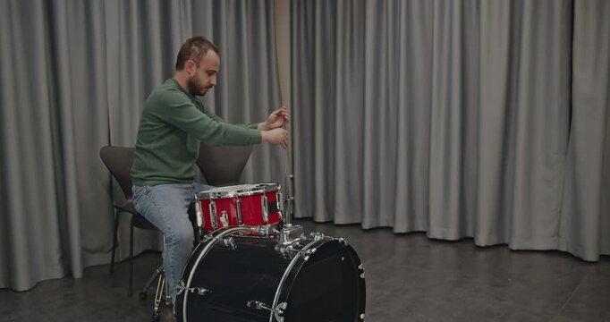 A drummer sets up his drum kit on a stage before a concert. He adjusts the snare and hi-hat, preparing for a music practice session.