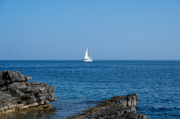 A sailing ship in the blue sea, rocks in the foreground