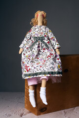 Handcrafted cloth doll in floral dress with bow, sitting on wooden box indoors