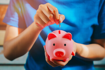 Saving money concept. Close-up of a person inserting a coin into a pink piggy bank symbolizing...