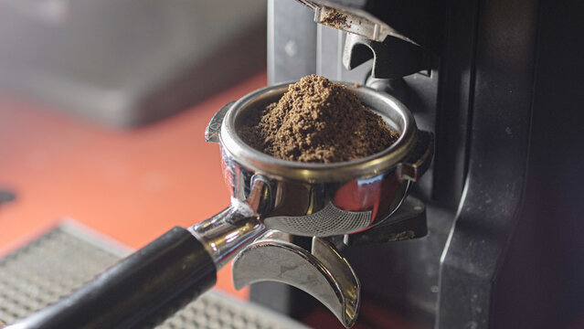 Coffee grinder grinds fresh coffee beans into a portafilter. Barista grind espresso coffee bean with grinder machine. Ambient light. Selective focus