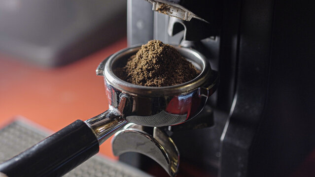 Coffee grinder grinds fresh coffee beans into a portafilter. Barista grind espresso coffee bean with grinder machine. Ambient light. Selective focus