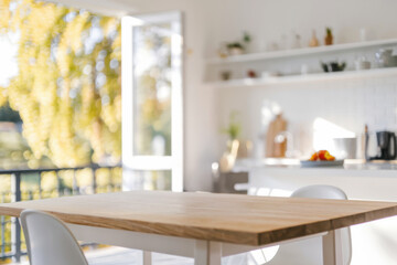 A warm and inviting modern kitchen interior with open balcony and wooden table under sunlight streaming from outside in the background, display product, mockup table
