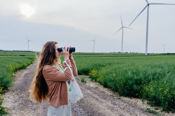 Woman with binoculars and mesh bag observing wind turbines