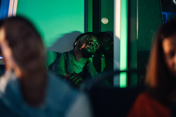 Young man relaxing listening to music on night bus illuminated by green neon lights
