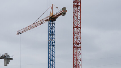 There are two construction cranes in the sky, one red and blue, and the other white. The sky is...