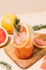 Grapefruit cocktail with rosemary garnish in a glass, served on a wooden cutting board. Vibrant,...