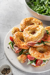 Homemade bagle sandwiches with ham, soft cheese and vegetables on whire board on kitchen table background. Homemade burgers