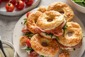 Homemade bagle sandwiches with ham, soft cheese and vegetables on whire board on kitchen table background. Homemade burgers