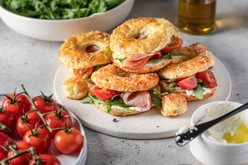 Homemade bagle sandwiches with ham, soft cheese and vegetables on whire board on kitchen table background. Homemade burgers