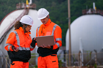 Two engineers in high-visibility safety gear and hard hats discuss project plans on a laptop in...