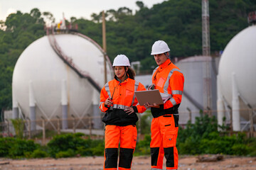 Two engineers in high-visibility safety gear and hard hats discuss project plans on a laptop in...