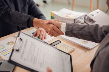 Real estate agent shaking hands with client after signing sales contract in office with house...
