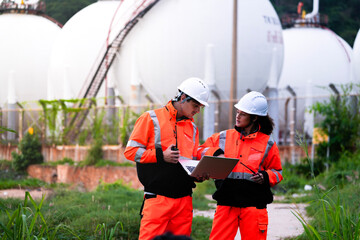 Two engineers in high-visibility safety gear and hard hats discuss project plans on a laptop in...