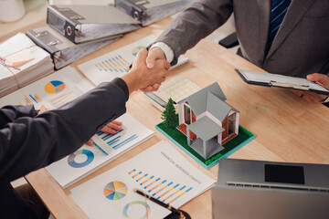 Real estate agent shaking hands with client after signing sales contract in office with house...