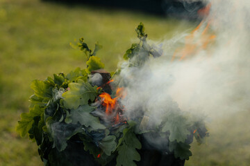 A metal fire basket with tall, bright orange flames burns on a grassy lawn, with embers rising into...
