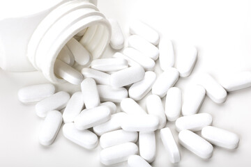 White tablets scattered on a white background. A bottle is tipped over, with several pills spilling...