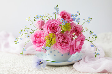Bouquet of spring and summer flowers in a cup on the table, rose, forget me not flowers, beautiful card, still life, blur.