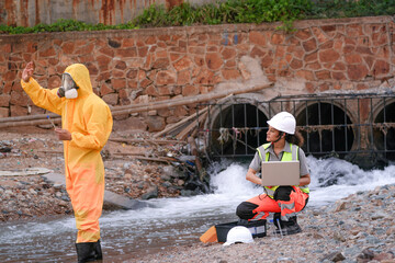 Environmental field team in protective gear analyzes water samples on a polluted beach. One holds a...