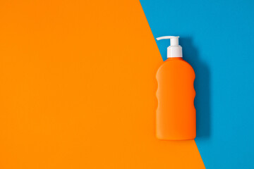 Bottle of orange sunscreen on blue and orange background. Sun cream.